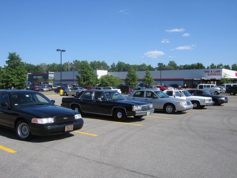 2001 Ford Crown Victoria - A row of sedans, including a black 2001 Ford Crown Victoria, are parked in a lot on a sunny day.
