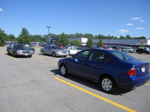 2001 Ford Crown Victoria - A blue sedan is parked in a lot with other vehicles under a clear blue sky.