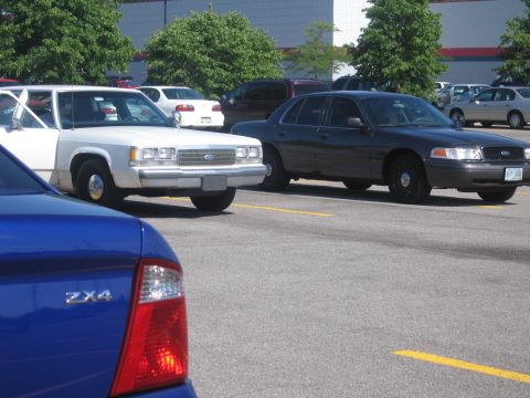 2001 Ford Crown Victoria - A dark gray 2001 Ford Crown Victoria police car is parked in a lot, with other vehicles visible.