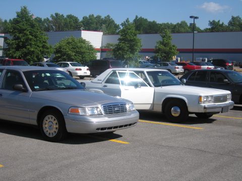 2001 Ford Crown Victoria - Two vehicles in a parking lot: a silver Ford Crown Victoria and a white custom pickup truck.
