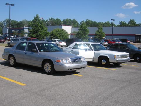 2001 Ford Crown Victoria - Two sedans are parked in a lot with a Walmart in the background.