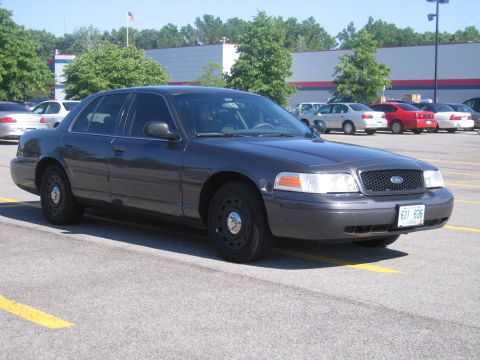 2001 Ford Crown Victoria - A dark gray 2001 Ford Crown Victoria is parked in a lot with other vehicles visible in the background.