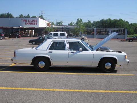 2001 Ford Crown Victoria - A white sedan is parked in a lot with its hood open. The vehicle's body style suggests it is from the 1990s.