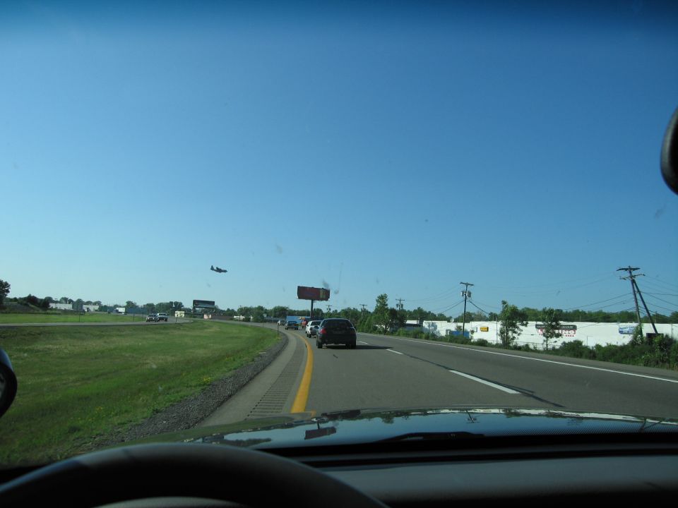 View from car dashboard looking at highway traffic and a distant airplane under a clear blue sky