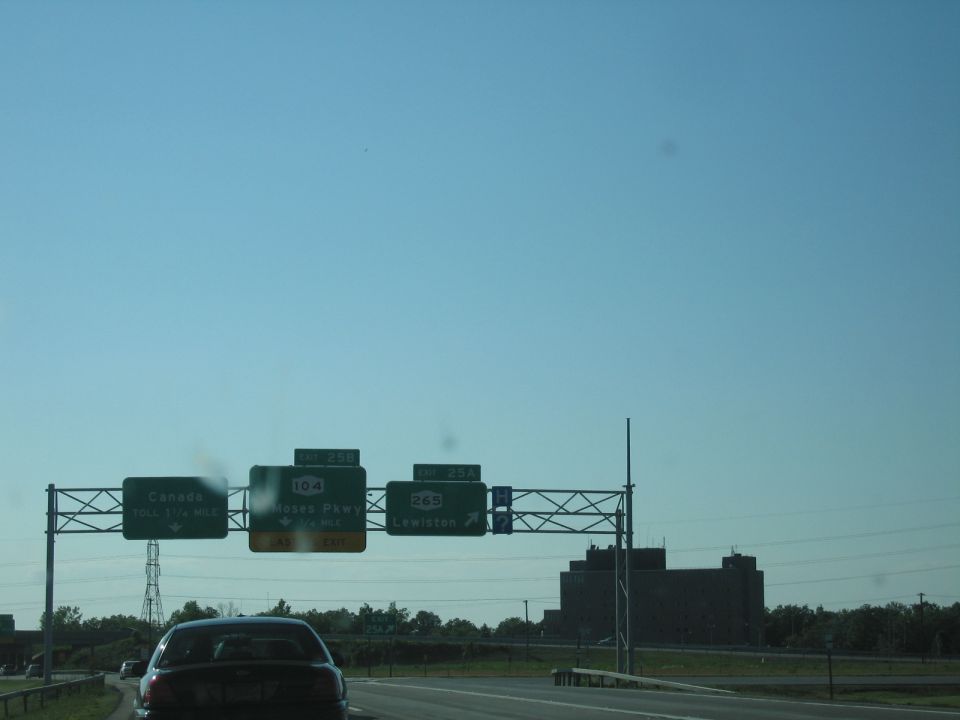 Dark sedan on highway approaching overhead signs for Canada, 104, Moses Pkwy, 265, and Lewiston