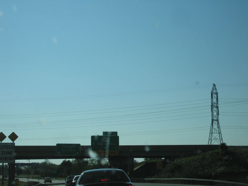 Cars on highway under overpass with power lines and a tall tower in the distance