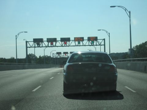 2001 Ford Crown Victoria - Rear view of a 2001 Ford Crown Victoria on a highway, approaching toll booths with lane indicators.