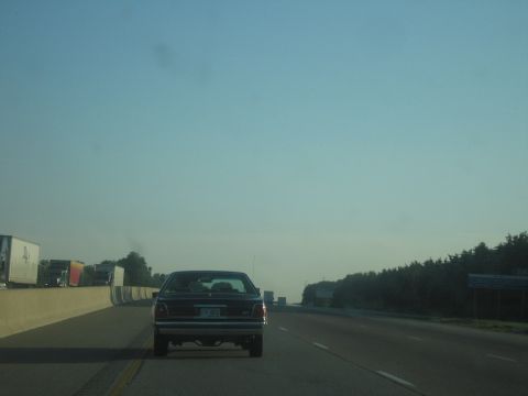 2001 Ford Crown Victoria - Rear view of a dark 2001 Ford Crown Victoria driving on a highway with other vehicles present.