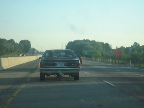 2001 Ford Crown Victoria - Rear view of a 2001 Ford Crown Victoria on the highway, with other vehicles visible.