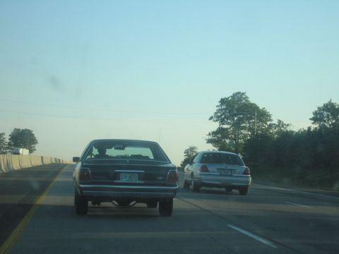2001 Ford Crown Victoria - Two sedans are traveling on a highway under a clear sky.