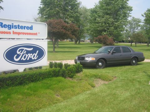 2001 Ford Crown Victoria - A dark gray 2001 Ford Crown Victoria is parked on the grass next to a large Ford sign.