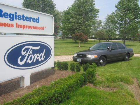 2001 Ford Crown Victoria - A Ford Crown Victoria is parked on a grassy lawn near a large Ford logo sign.