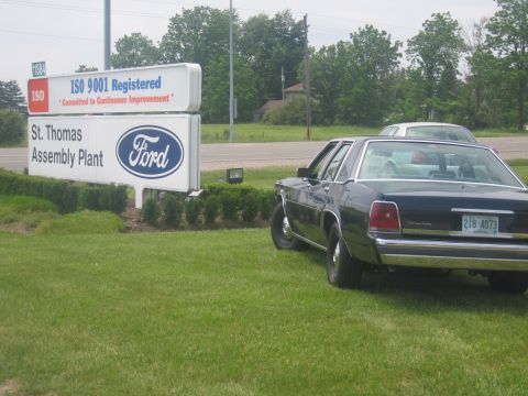 2001 Ford Crown Victoria - A dark sedan is parked on the grass next to the St. Thomas Assembly Plant sign.