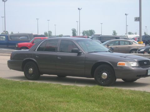 2001 Ford Crown Victoria - Side view of a dark gray 2001 Ford Crown Victoria sedan parked in a lot with other vehicles.