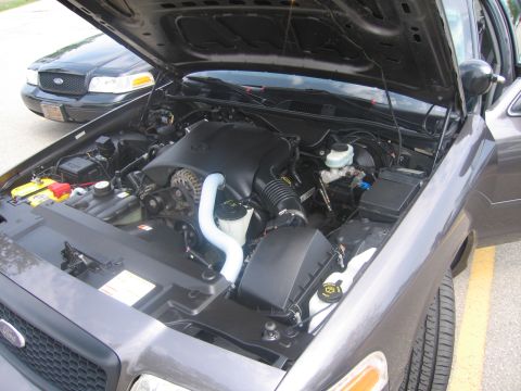 2001 Ford Crown Victoria - Engine bay of a grey sedan, with a black sedan visible in the background.