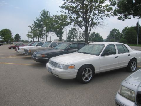 2001 Ford Crown Victoria - Several sedans are parked in an outdoor lot under a cloudy sky.