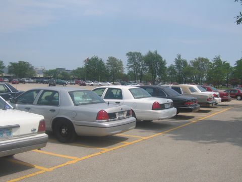 2001 Ford Crown Victoria - A silver 2001 Ford Crown Victoria is parked in a lot alongside several other vehicles under a partly cloudy sky.