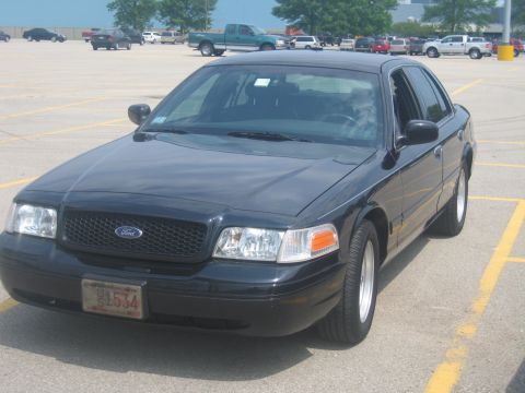 2001 Ford Crown Victoria - A black 2001 Ford Crown Victoria is parked in a lot with other vehicles in the background.