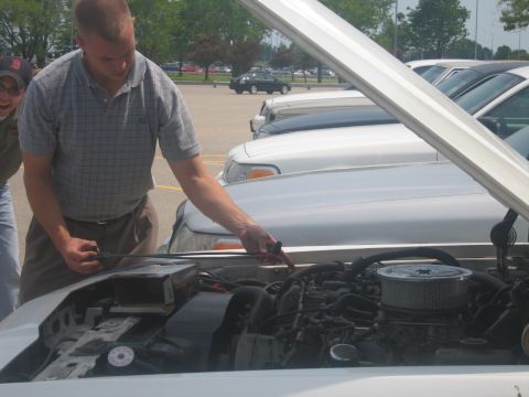 2001 Ford Crown Victoria - A man inspects the engine of a white 2001 Ford Crown Victoria parked in a lot.