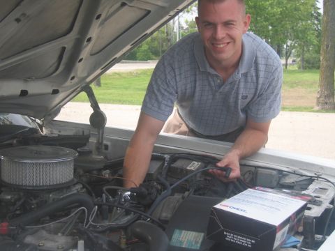 2001 Ford Crown Victoria - A man works on the engine of a car, holding a spark plug wire near a box of CarQuest parts.