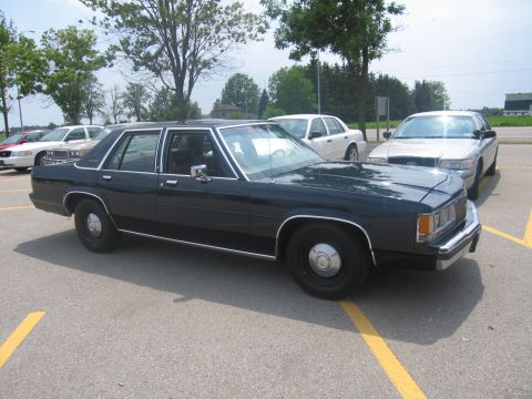 2001 Ford Crown Victoria - A dark sedan is parked in a lot with other vehicles visible in the background.