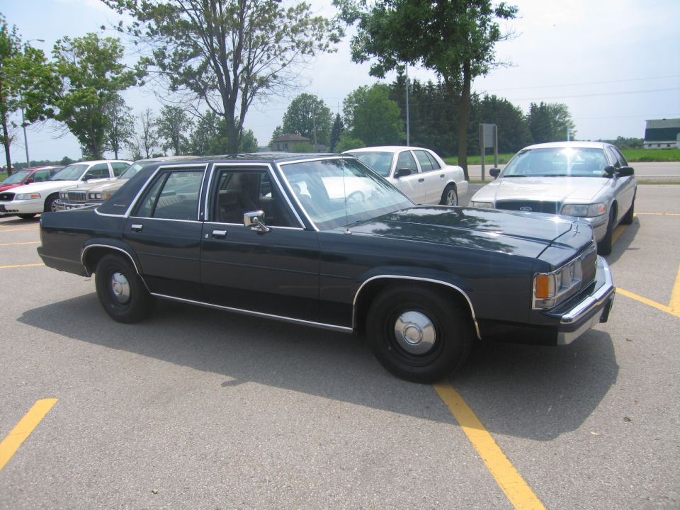 Dark sedan parked in a lot, with other cars behind it. The sedan has chrome trim and hubcaps