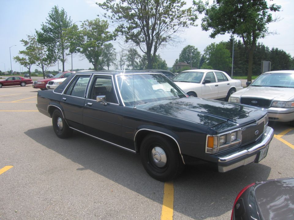 Dark sedan parked in a lot, front quarter view. Other cars are visible in the background