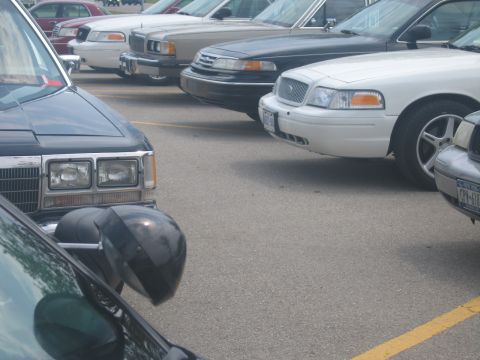2001 Ford Crown Victoria - Multiple sedans are parked in a lot, including a white 2001 Ford Crown Victoria.