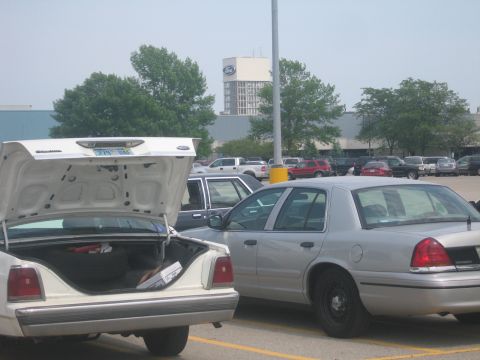 2001 Ford Crown Victoria - Parking lot scene with multiple vehicles, including a silver 2001 Ford Crown Victoria and a white car with its trunk open.