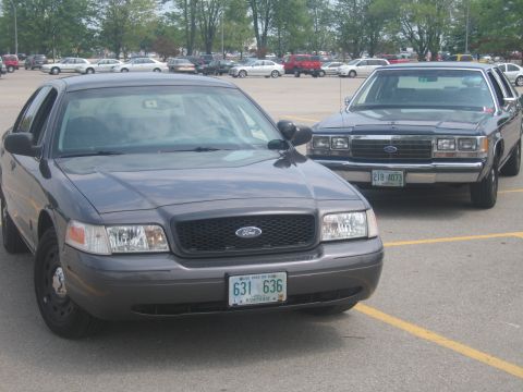 2001 Ford Crown Victoria - Two Ford Crown Victorias, one newer and one older model, parked side-by-side in a parking lot.