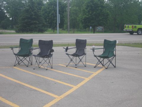 2001 Ford Crown Victoria - Four folding chairs are set up in parking spaces, with a green truck visible on the road in the distance.