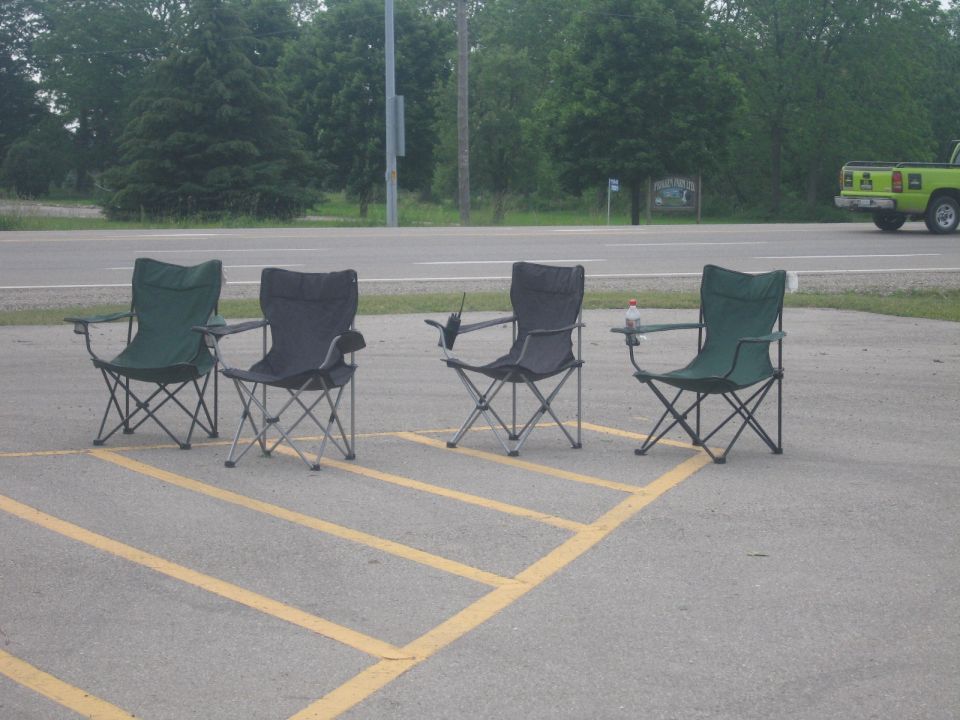 Four folding chairs in parking spaces with a green truck in the background