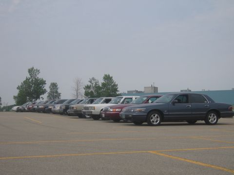 2001 Ford Crown Victoria - A row of sedans are parked in an outdoor lot under a cloudy sky.