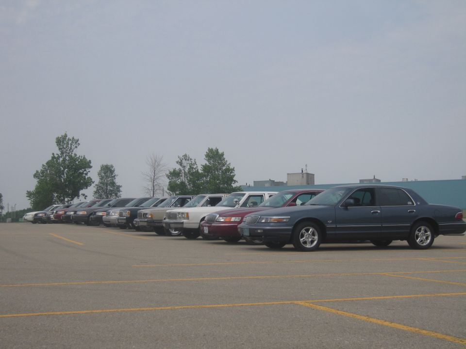 Several sedans parked in a lot, mostly dark colors, with a few lighter ones mixed in. The closest car is dark blue