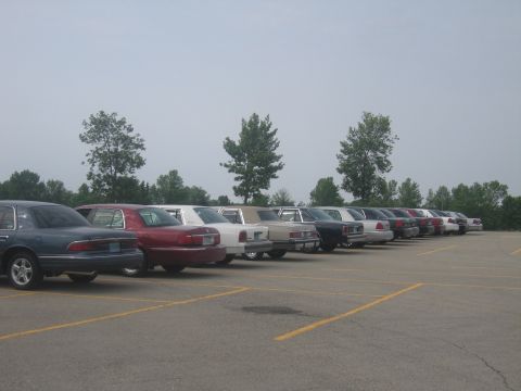 2001 Ford Crown Victoria - Multiple sedans are parked in a lot under an overcast sky.