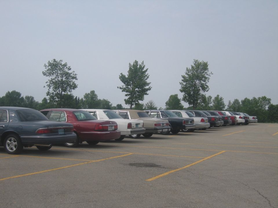 Line of sedans parked in a lot, viewed from the side; a dark blue sedan is in the foreground