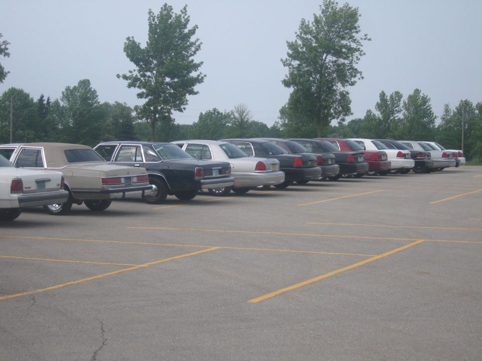 Line of sedans, including a 2001 Ford Crown Victoria, parked in a lot