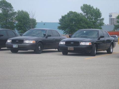 2001 Ford Crown Victoria - Two Ford Crown Victoria sedans, likely police vehicles, are parked side-by-side in an outdoor lot.