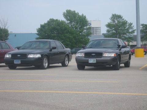 2001 Ford Crown Victoria - Two Ford Crown Victorias are parked side-by-side in a parking lot under an overcast sky.