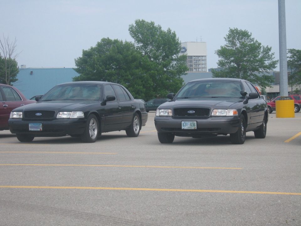 Two black Ford Crown Victorias parked in a lot, one slightly ahead of the other
