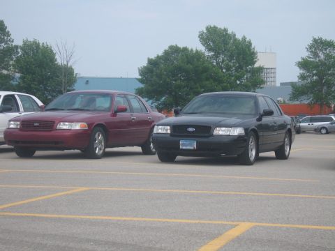 2001 Ford Crown Victoria - Two Ford Crown Victorias, one black and one red, are parked side-by-side in a parking lot. The black car has a license plate visible.