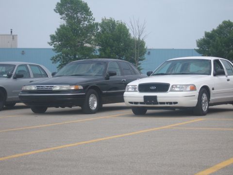 2001 Ford Crown Victoria - Two Ford Crown Victorias are parked side-by-side in a parking lot under an overcast sky.