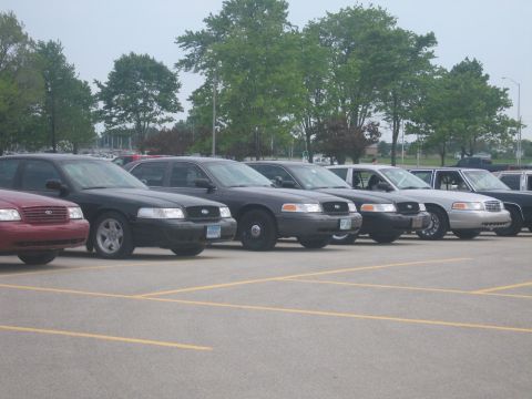 2001 Ford Crown Victoria - A line of police cruisers are parked in an outdoor lot under an overcast sky.