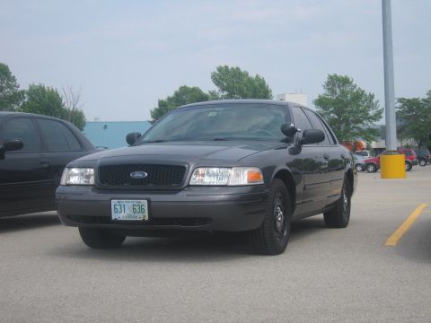 2001 Ford Crown Victoria - A dark gray 2001 Ford Crown Victoria police car is parked in a lot, with another vehicle to its left.