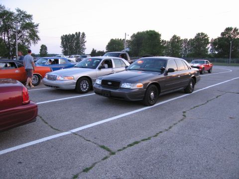 2001 Ford Crown Victoria - Photo of several cars parked in a paved lot at dusk, led by a Ford Crown Victoria.