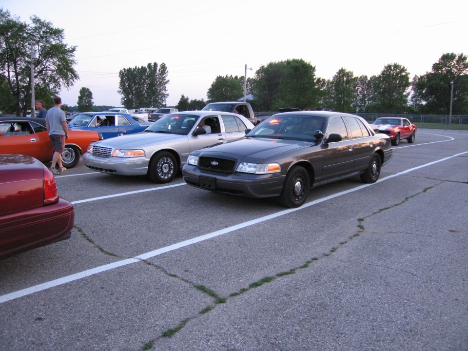 Row of cars including a Ford Crown Victoria in a paved lot at dusk