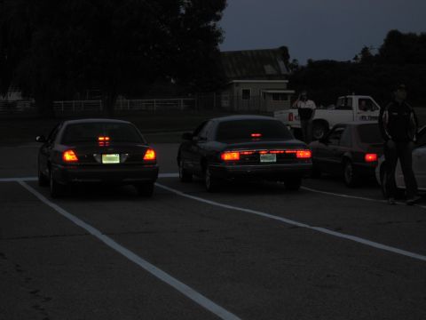 2001 Ford Crown Victoria - Photo of several cars from the rear with taillights illuminated in a lot at nightfall.