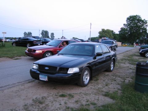 2001 Ford Crown Victoria - A black 2001 Ford Crown Victoria is parked on a dirt lot with other vehicles visible in the background.
