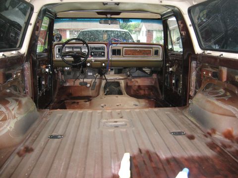 1979 Ford Bronco - The interior of a vehicle shows a dashboard and empty cargo area, with visible rust and stripped panels.
