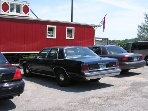 2001 Ford Crown Victoria - Rear view of a black 2001 Ford Crown Victoria parked in front of a red caboose-style building.